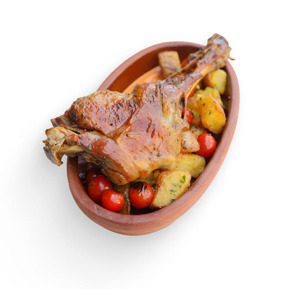 Roasted suckling lamb leg in an oval terra cotta dish with cherry tomatoes and potatoes